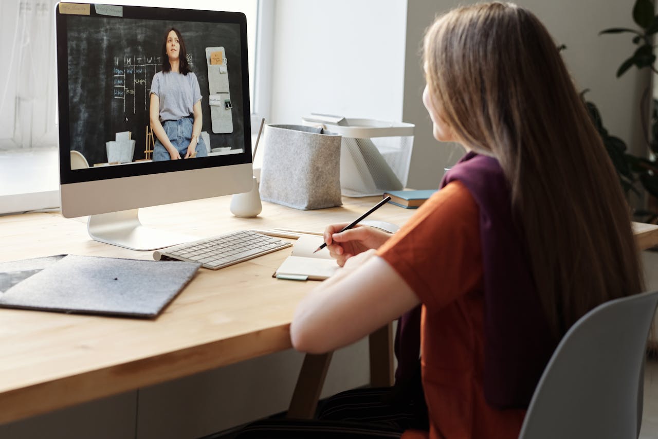 Services Teen girl attending an online class at home, takes notes at her desk.